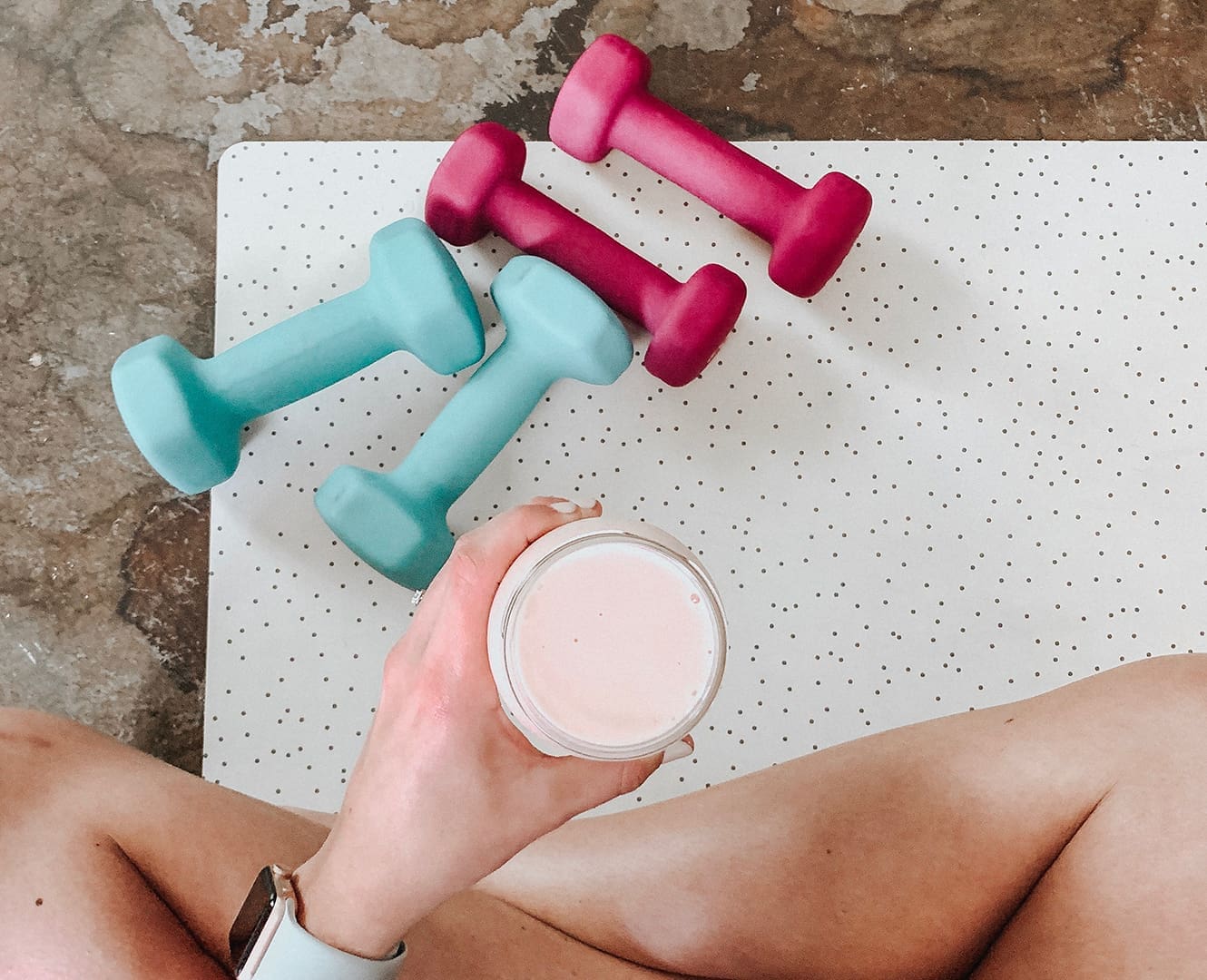Woman sitting on floor with smoothie and hand weights