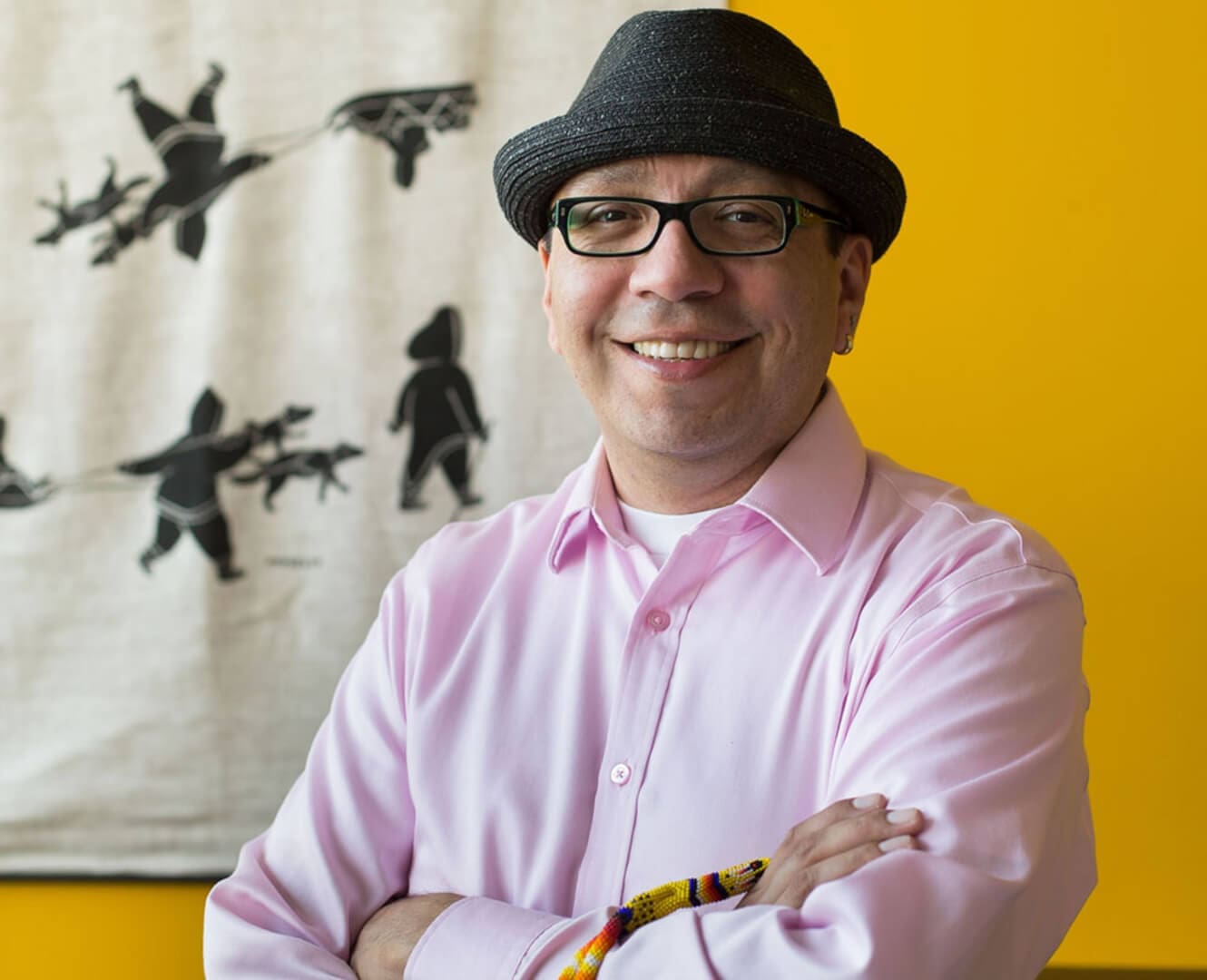 Derek Thunder Manager of Nîsôhkamâtotân Centre NAIT Aboriginal man stands wearing fedora hat against yellow backdrop