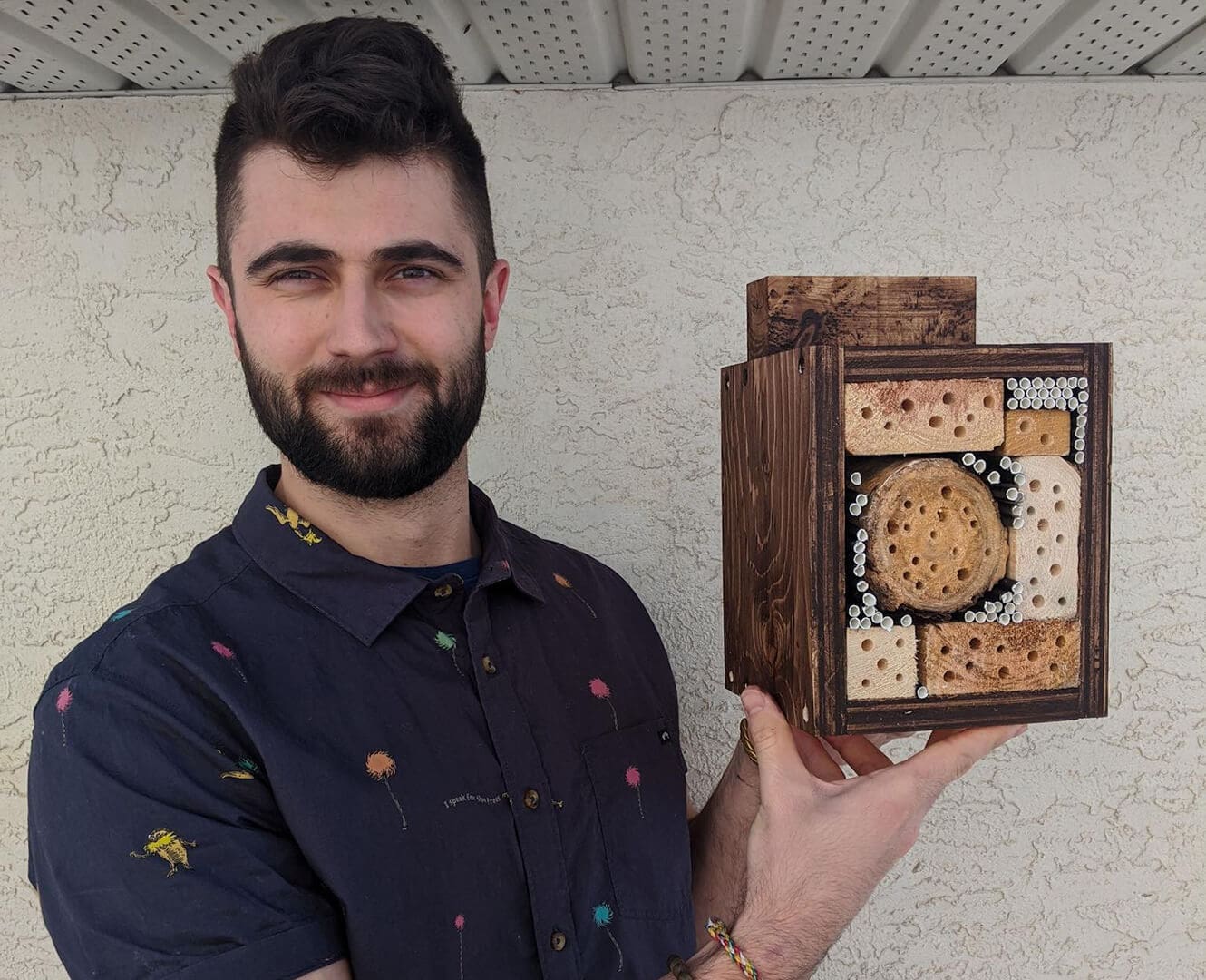 NAIT Club Saving the bees one hotel at a time Man holds handmade bee hotel.