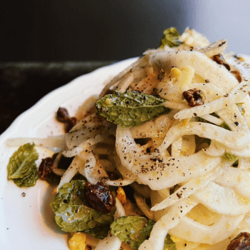 a pile of pasta on a white plate. there are small leaves, pepper and other garnishes on the pasta.