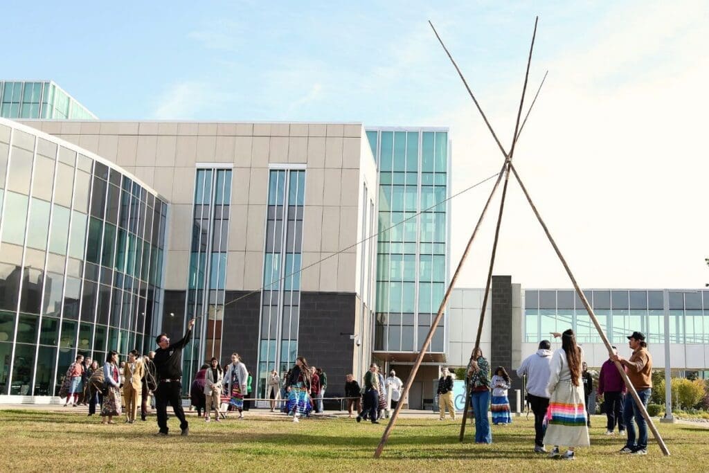 Photograph of a Tipi being raised and tied together during Treaty Day on campus outside of NAIT Feltham centre.