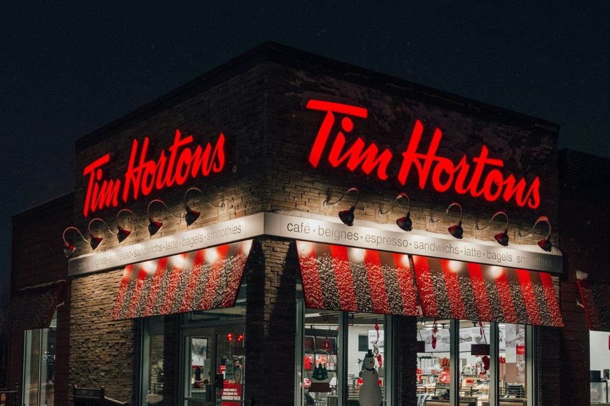 Image of a the exterior of a Tim Hortons restaurant at night. the red light from the logo and white lights from the restaurant wall lights illuminate the interior of the restaurant.