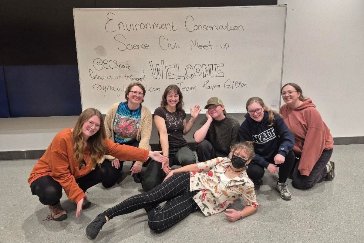 image of people inside the ECS club, sitting and posing in front of a whiteboard displaying the club name,