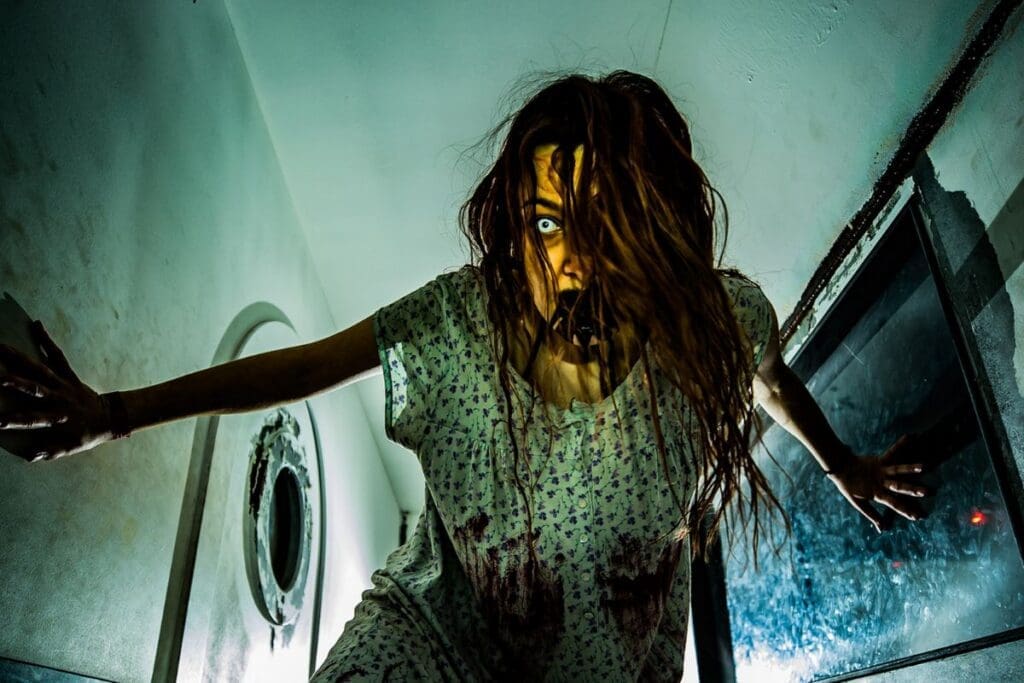 Feature image, photograph of a Deadmonton scare actor, clothed with a dirty white rag dress, dishelevel hair and a mutilated face mask looking down towards the camera.